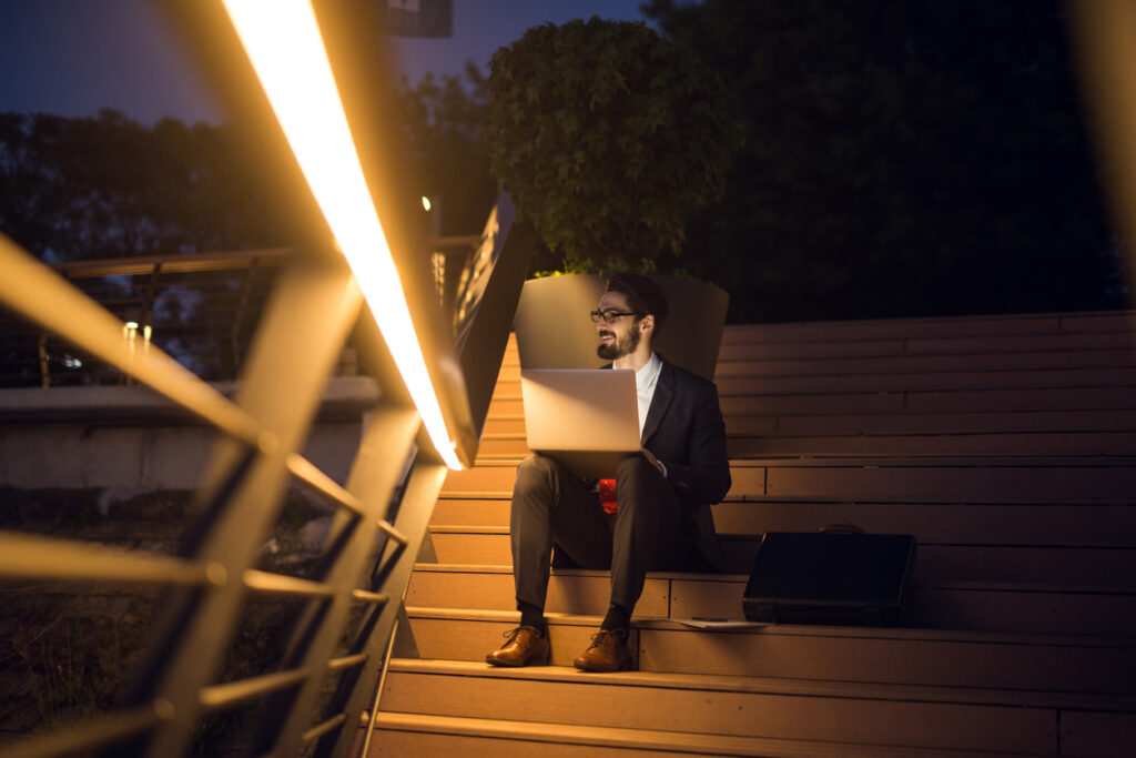 A man gives good feedback on content amends while working late. Sitting on stairs with laptop