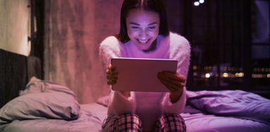Young woman sitting on bed with tablet reading about tone of voice