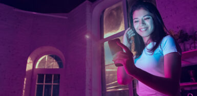 Portrait of stylish woman in neon lighted interior. Toned like cinema effects in purple-blue. Caucasian female model using smartphone in colourful lights indoors.